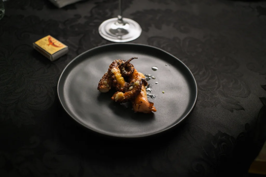 The octopus first course arranged on a dark plate at the dinner table